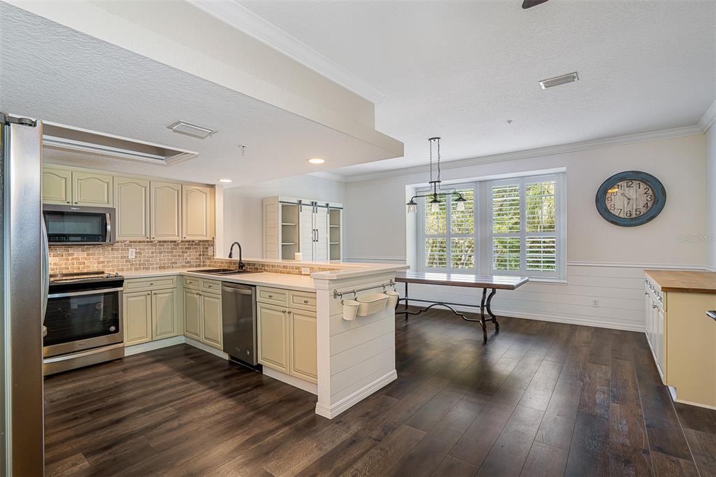 A kitchen with cream cabinets, stainless steel appliances, and a dining area with plantation shutters — 1381 CURLEW ROAD, DUNEDIN, FL
