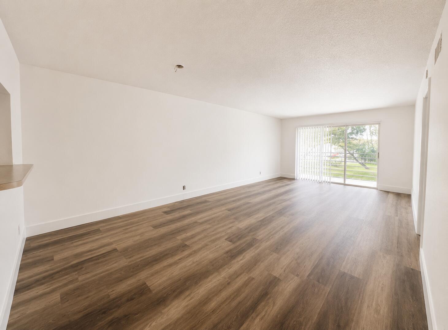 An empty living room with wood-look flooring, white walls, and a sliding glass door — 601 S State Rd 7 # 2h, Margate FL 33068, MARGATE, FL