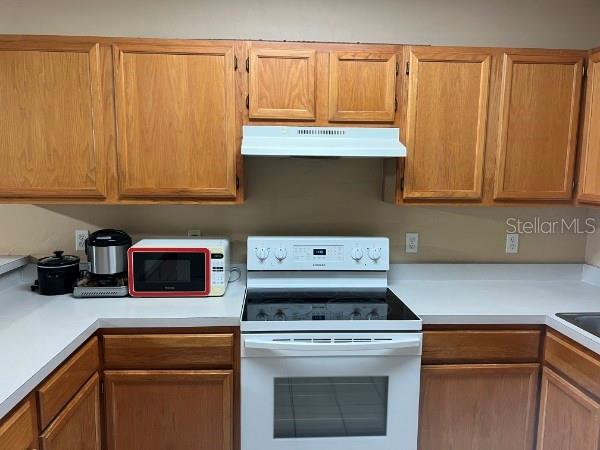 A kitchen features oak cabinets, a white range, a microwave, and a white countertop — 4415 SW 34TH STREET UNIT 608, GAINESVILLE, FL