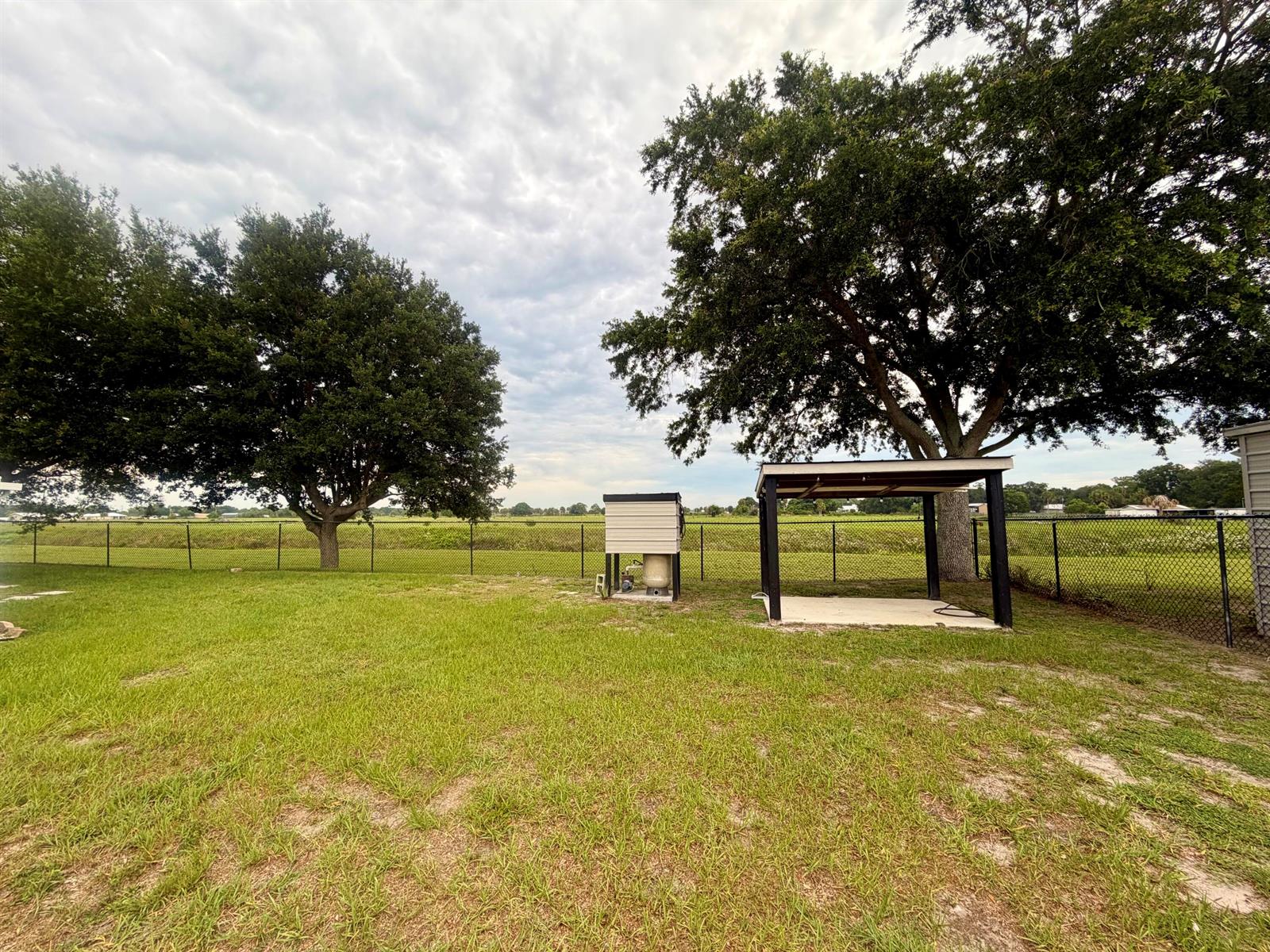A grassy backyard features a small utility shed, a covered patio, and mature trees — 7823 SW 9th Street, Okeechobee FL 34974, OKEECHOBEE, FL