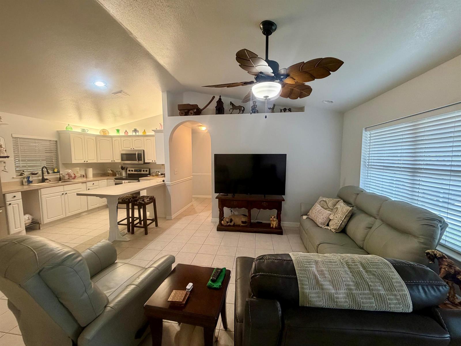 A living room with a ceiling fan, television, and an open kitchen with white cabinets — 7823 SW 9th Street, Okeechobee FL 34974, OKEECHOBEE, FL