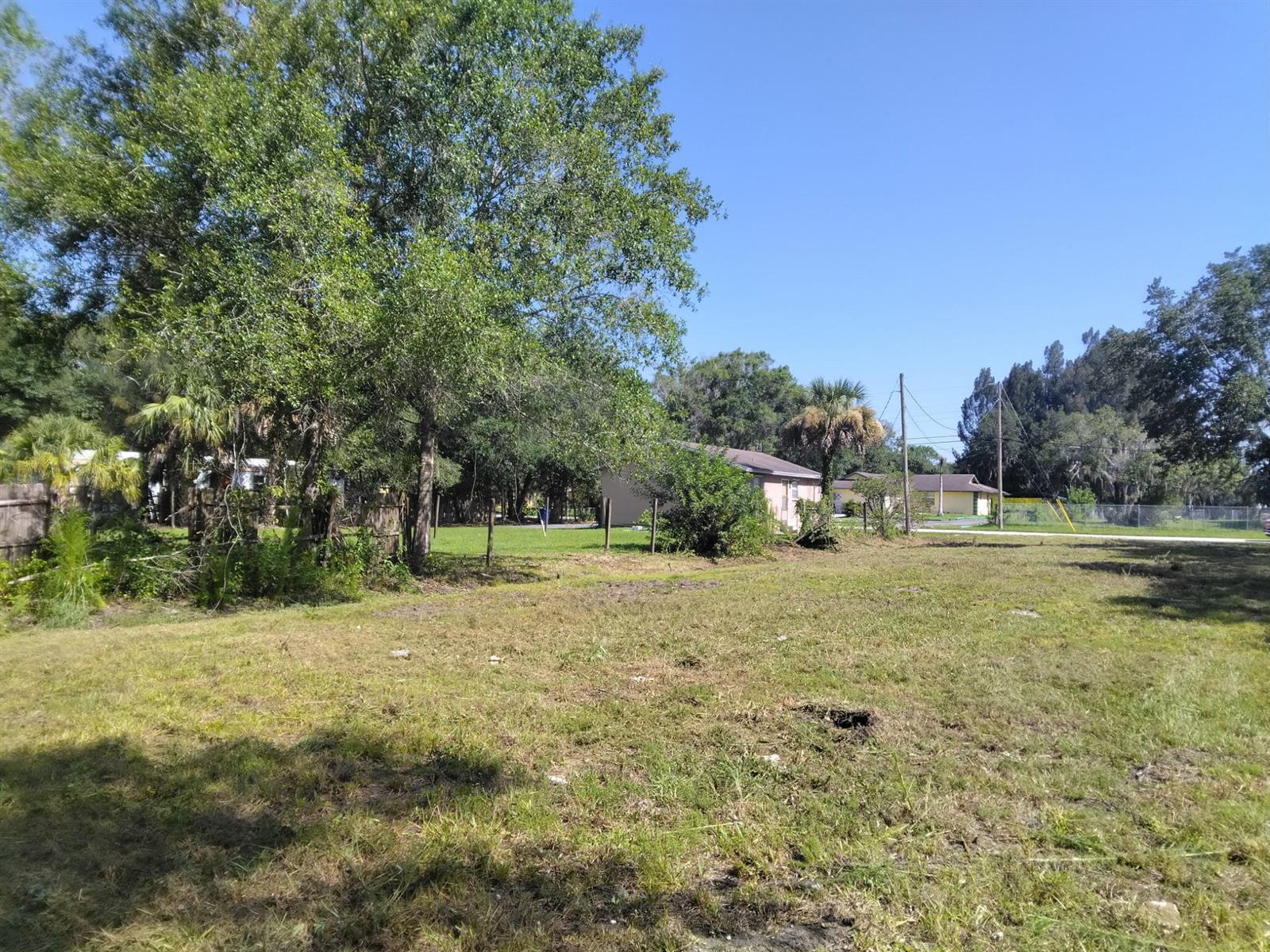 A grassy, partially shaded lot with trees and neighboring houses in the background — FELLSMERE, FL