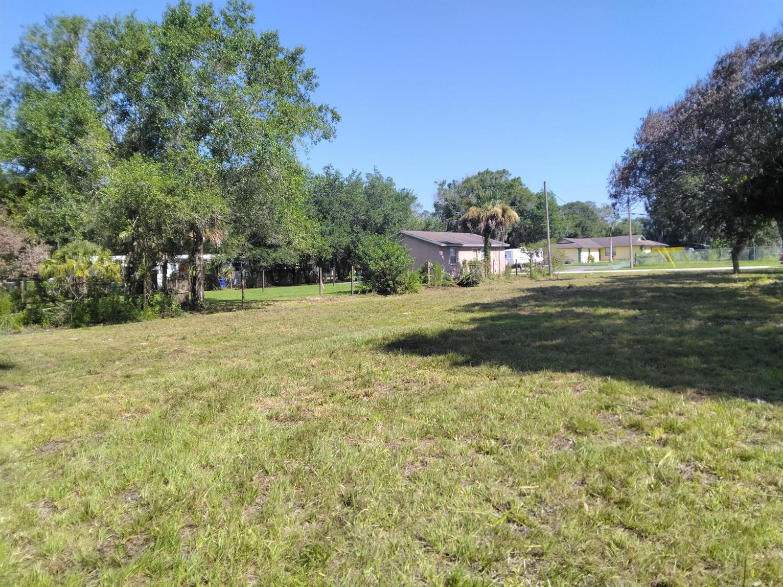 A grassy, vacant lot with trees and neighboring houses in the background under a blue sky — FELLSMERE, FL
