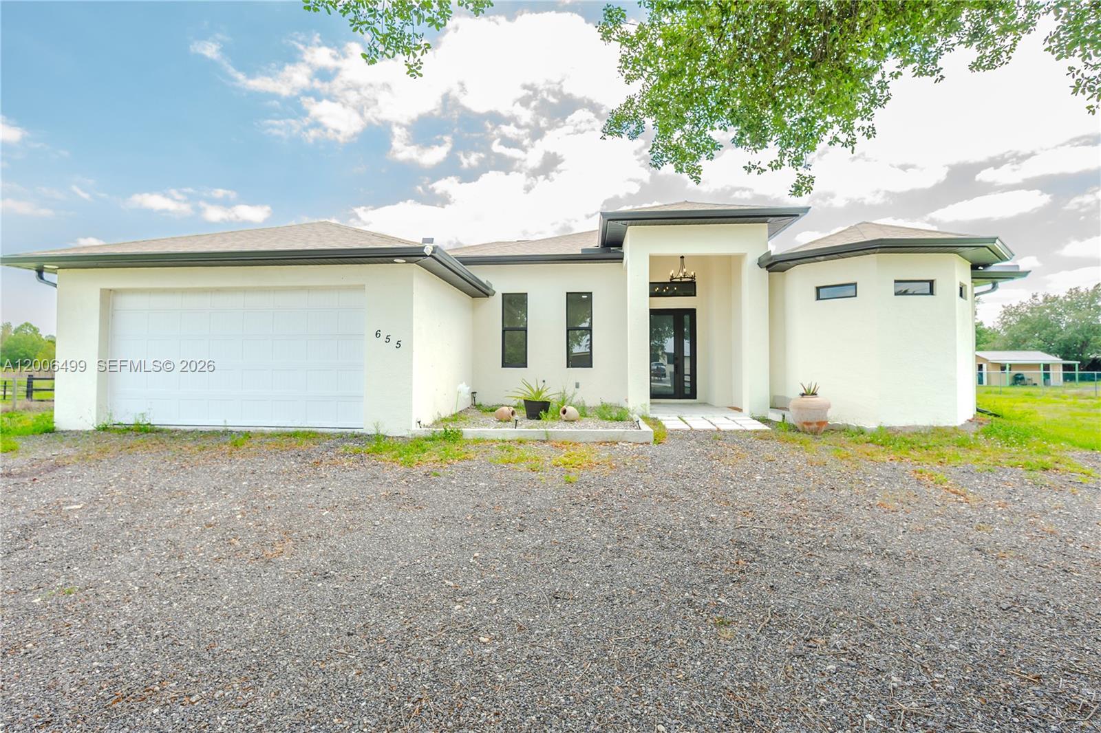 A single-story house with a white stucco exterior, a gravel driveway, and a two-car garage — 655 N Olivo ST, Clewiston FL 33440, CLEWISTON, FL