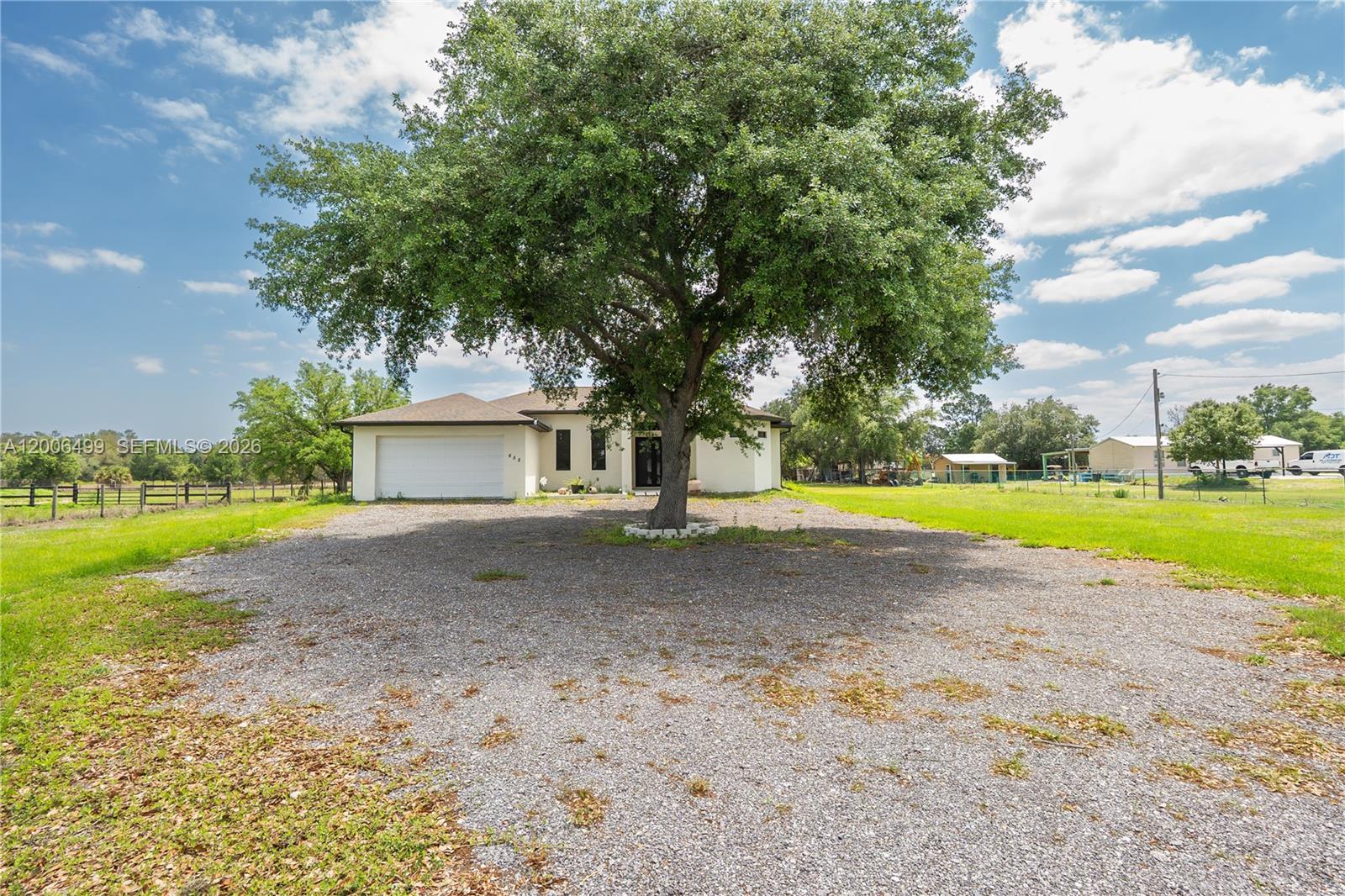 A single-story house with a white exterior and a large tree in the gravel driveway — 655 N Olivo ST, Clewiston FL 33440, CLEWISTON, FL