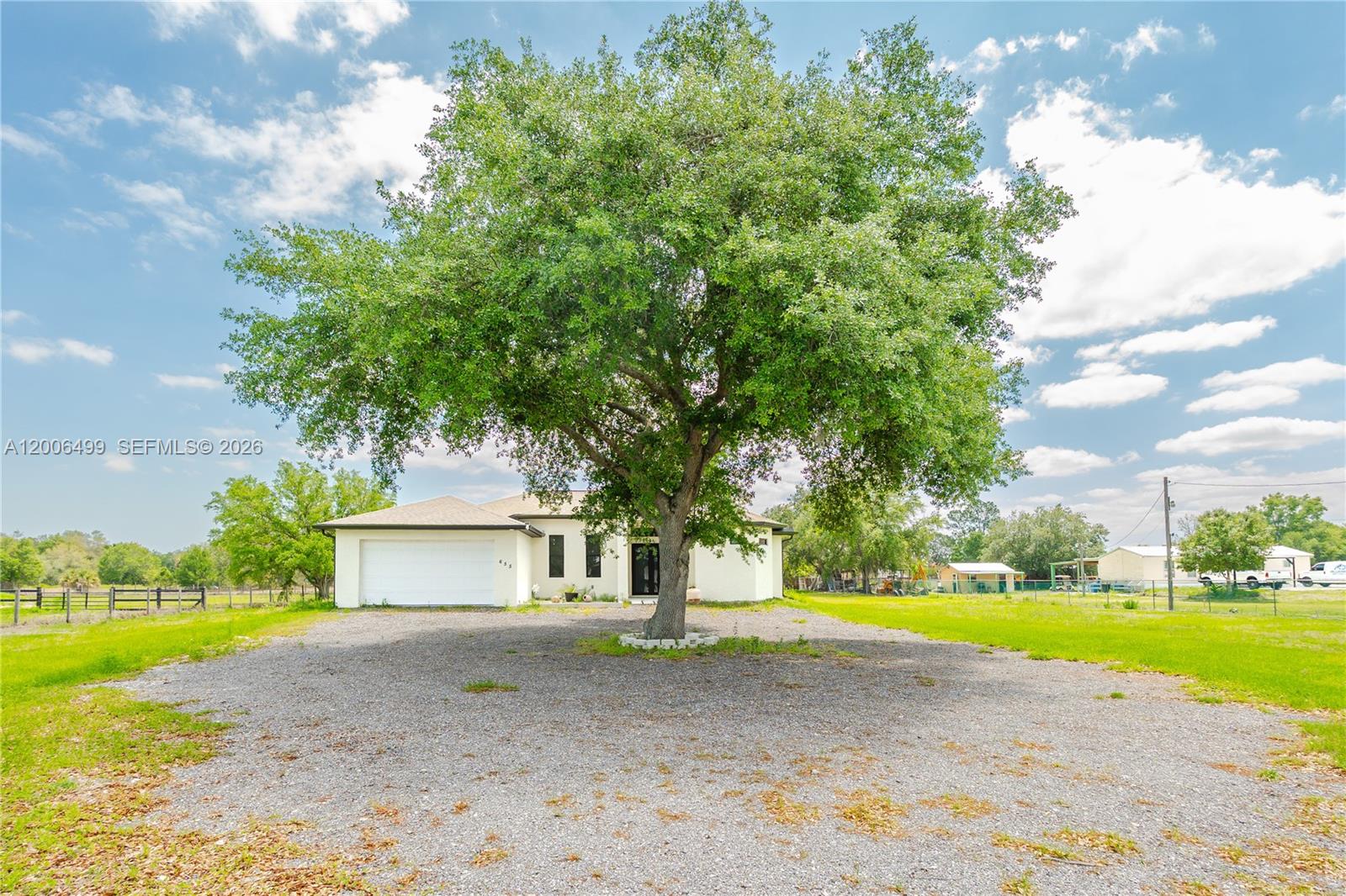 A large tree stands in the center of a gravel driveway in front of a house — 655 N Olivo ST, Clewiston FL 33440, CLEWISTON, FL