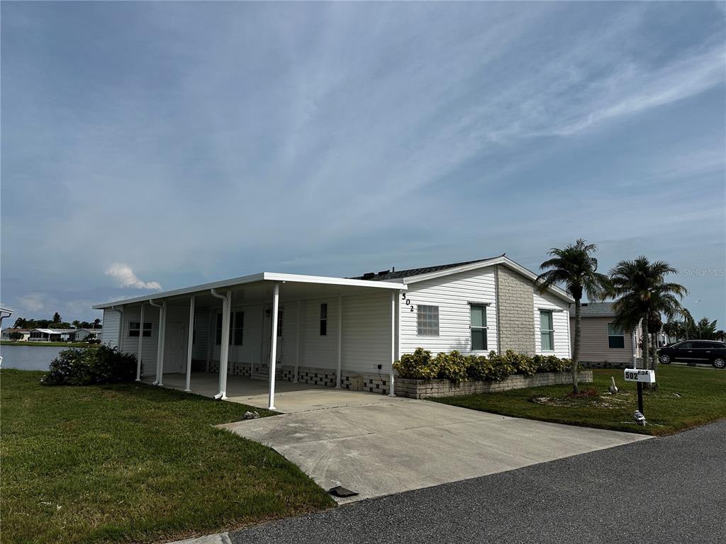 A white manufactured home with a carport and a concrete driveway sits near a lake — 502 AMBERJACK DRIVE, NORTH PORT, FL