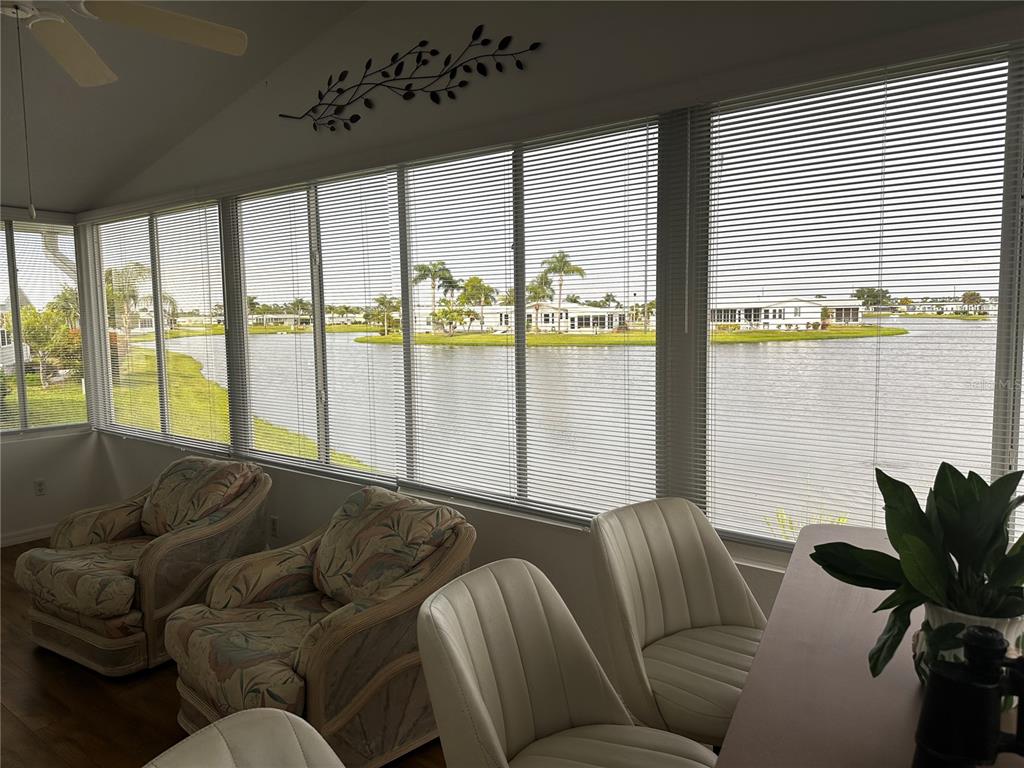 A sunroom with patterned armchairs and white chairs overlooks a lake and neighboring houses — 502 AMBERJACK DRIVE, NORTH PORT, FL