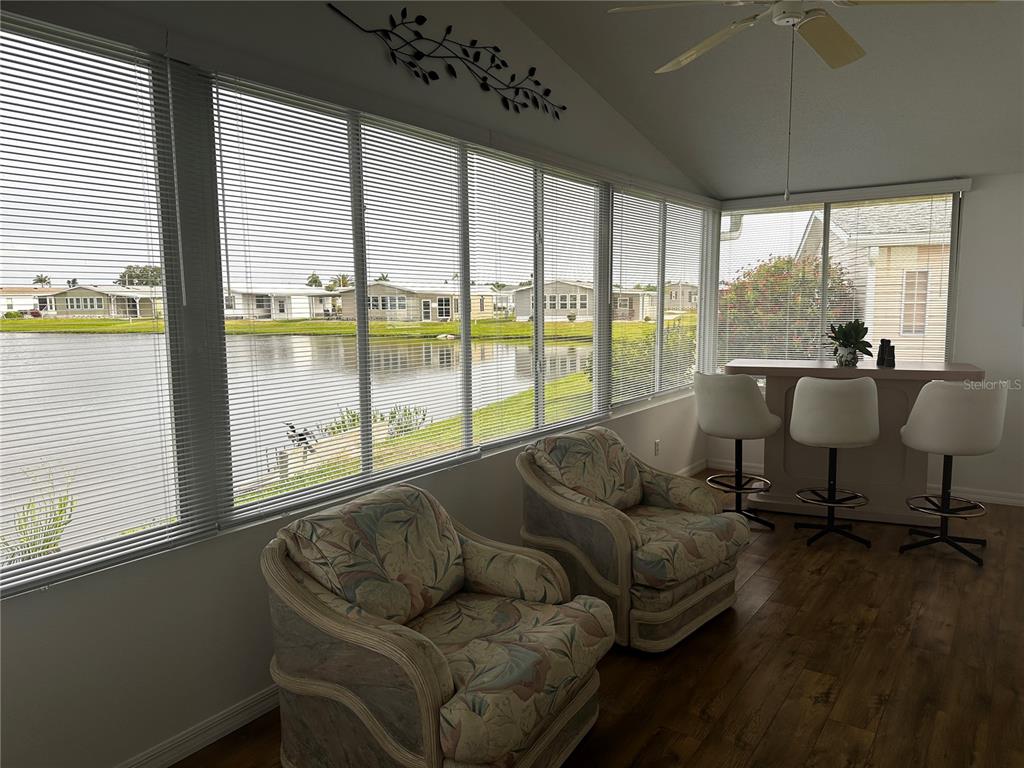 A sunroom with floral armchairs, a bar with stools, and large windows overlooking a lake — 502 AMBERJACK DRIVE, NORTH PORT, FL