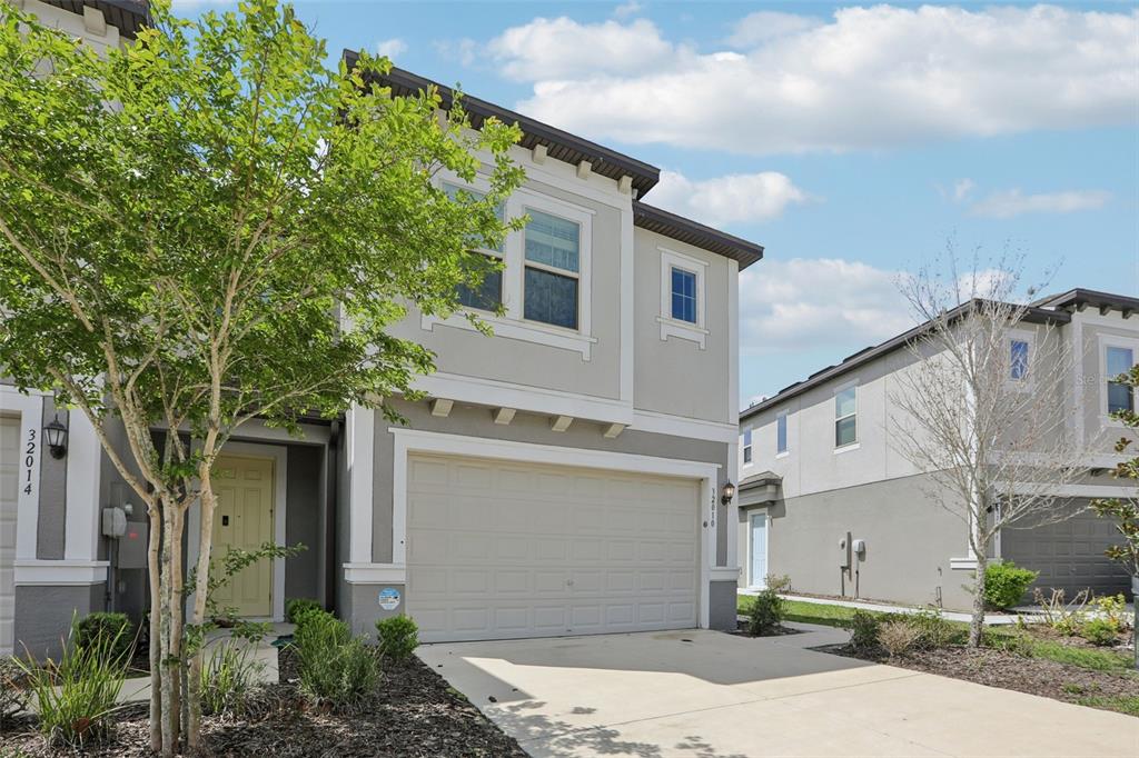 A two-story suburban house with a beige stucco exterior, a two-car garage, and a driveway — 32010 BLUE PASSING LOOP, WESLEY CHAPEL, FL