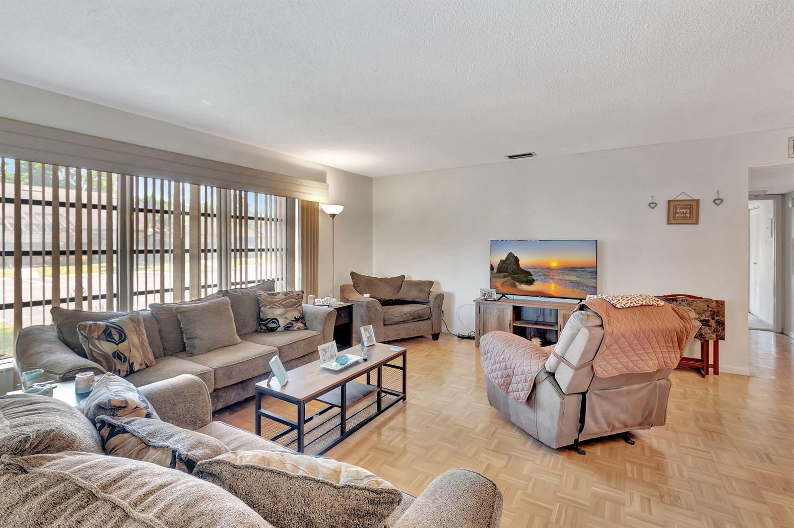 A living room features a sectional sofa, a recliner, a television, and light wood flooring — 14110 Nesting Way # A, Delray Beach FL 33484, DELRAY BEACH, FL