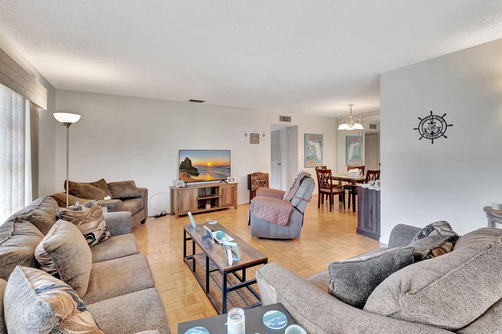 A living room with light wood parquet flooring, brown furniture, and an adjacent dining area — 14110 Nesting Way # A, Delray Beach FL 33484, DELRAY BEACH, FL