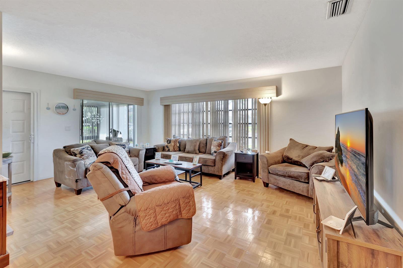 A living room features light wood parquet flooring, a brown sofa set, and a television — 14110 Nesting Way # A, Delray Beach FL 33484, DELRAY BEACH, FL