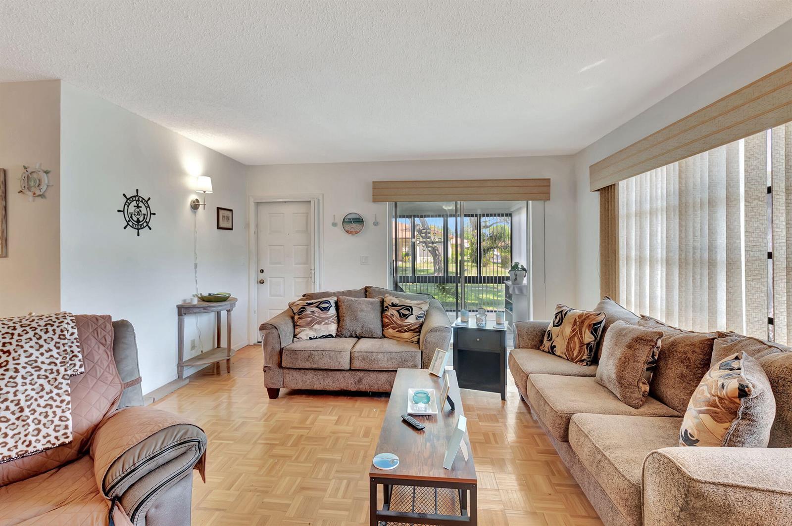 A living room features light wood parquet flooring, a brown sofa set, and sliding glass doors — 14110 Nesting Way # A, Delray Beach FL 33484, DELRAY BEACH, FL