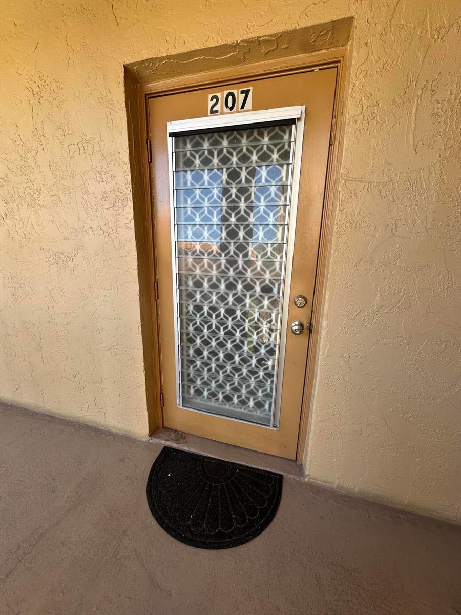 A tan exterior door labeled 207 features a decorative glass insert and a black doormat — 6770 Royal Palm Boulevard # 207l, Margate FL 33063, MARGATE, FL