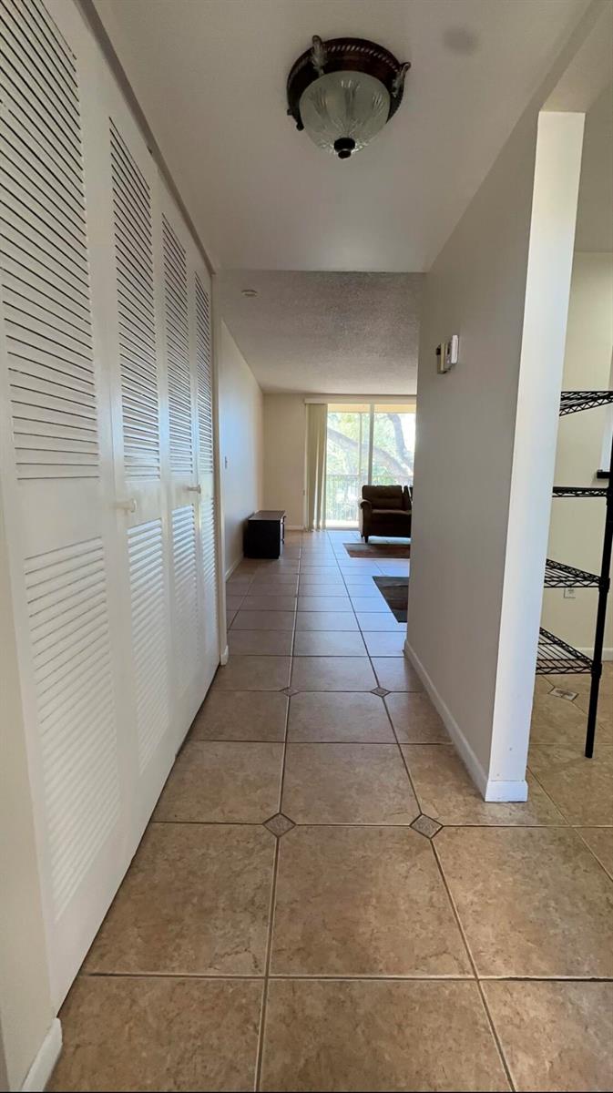 A tiled hallway leads past louvered closet doors toward a living area with balcony access — 6770 Royal Palm Boulevard # 207l, Margate FL 33063, MARGATE, FL