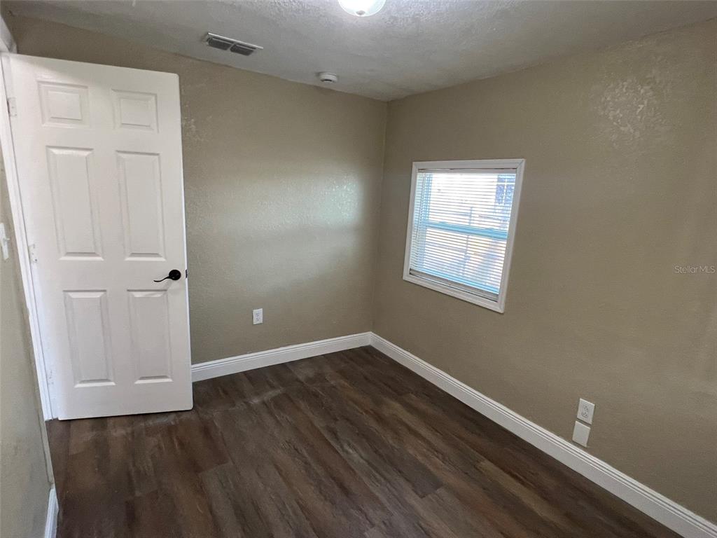 An empty bedroom features tan walls, white trim, a white door, and dark wood-look flooring — 1307 W KALEY AVENUE, ORLANDO, FL