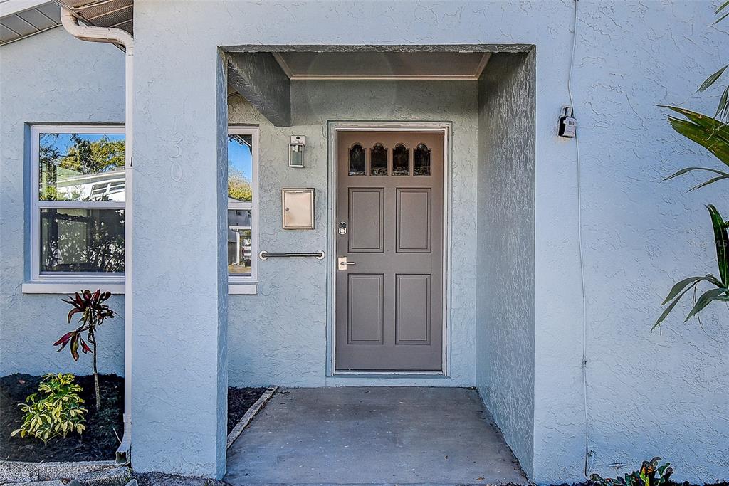 A light blue exterior wall features a gray front door with four glass panels above — 130 42ND AVENUE N, ST PETERSBURG, FL