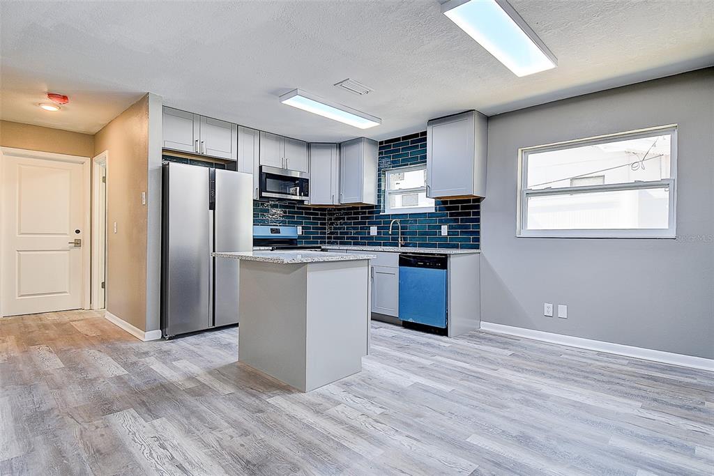 A kitchen features gray cabinets, a small island, stainless steel appliances, and blue tile backsplash — 130 42ND AVENUE N, ST PETERSBURG, FL