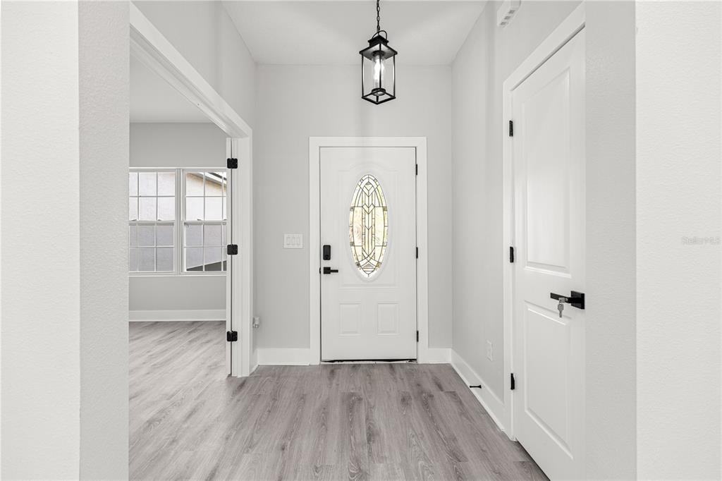 An entryway features light wood-look flooring, a white front door with glass, and a pendant light — 8311 SW 136TH TERRACE, DUNNELLON, FL