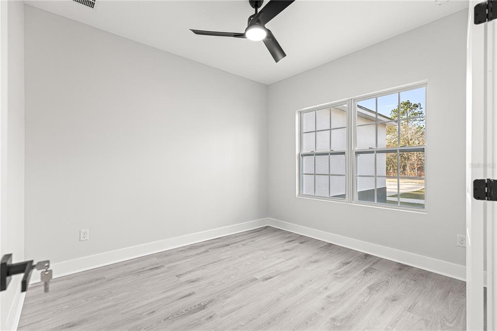 An empty bedroom features light gray walls, wood-look flooring, a ceiling fan, and a window — 8311 SW 136TH TERRACE, DUNNELLON, FL