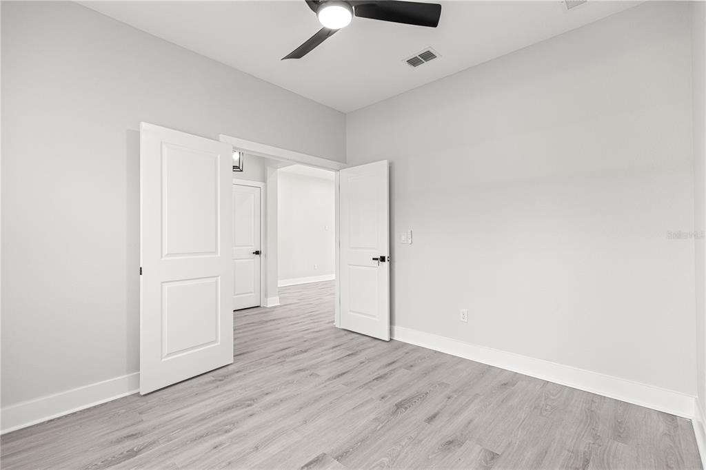 A room with light gray walls, wood-look flooring, a ceiling fan, and double doors — 8311 SW 136TH TERRACE, DUNNELLON, FL