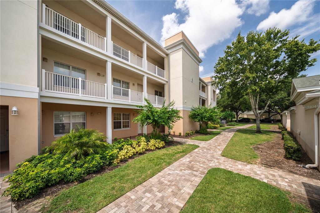 A three-story apartment building with balconies and a paved walkway through a landscaped courtyard — 7503 MOURNING DOVE CIR UNIT 202, REUNION, FL