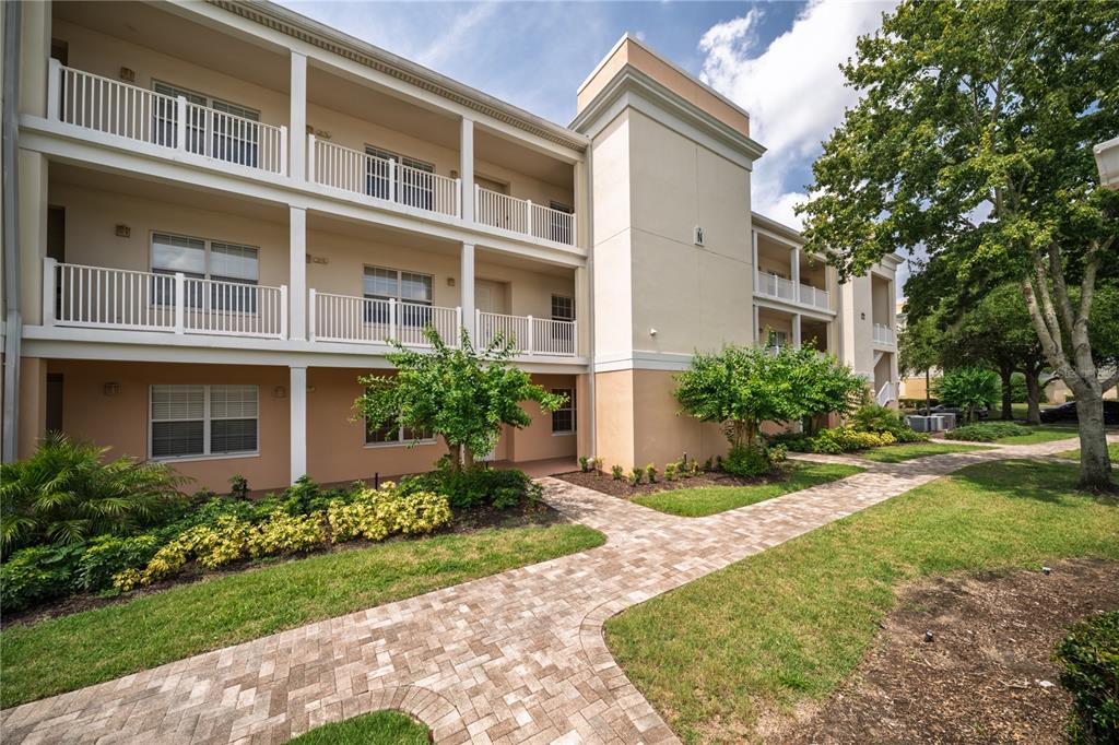 A three-story apartment building with white railings, tan stucco walls, and a brick walkway — 7503 MOURNING DOVE CIR UNIT 202, REUNION, FL