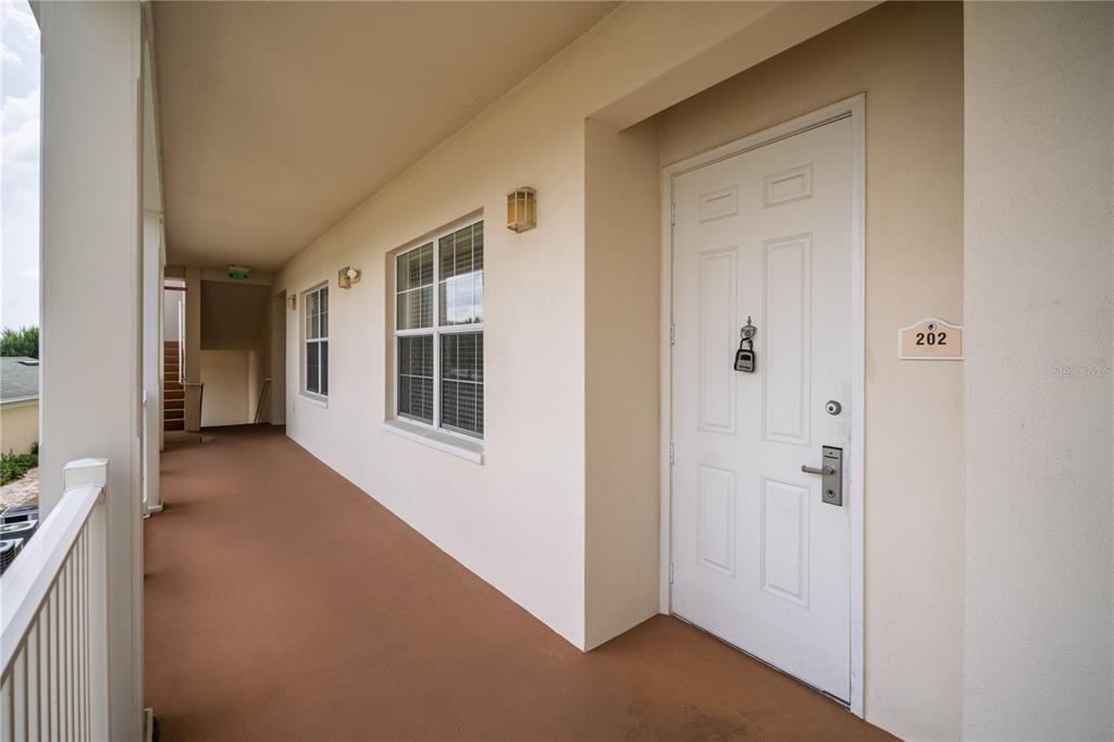 An exterior walkway leads to the white front door of unit 202 — 7503 MOURNING DOVE CIR UNIT 202, REUNION, FL