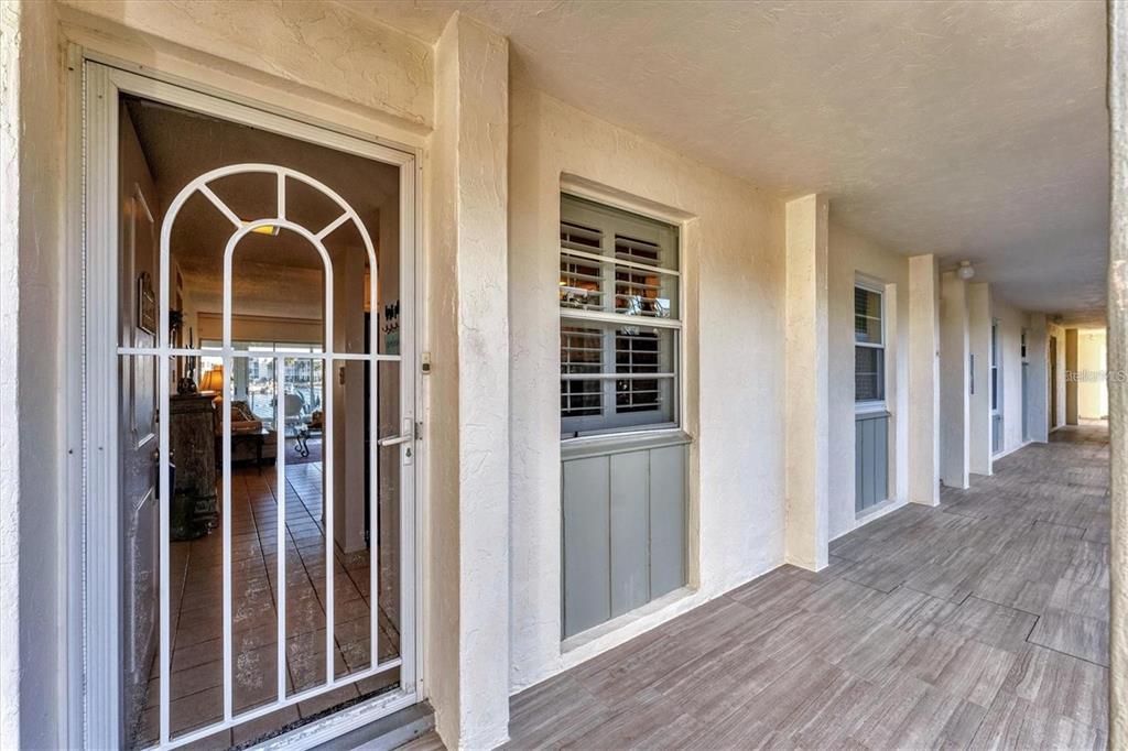 An exterior walkway features tiled flooring, white stucco walls, and a white arched screen door — 4350 CHATHAM DRIVE UNIT 106, LONGBOAT KEY, FL