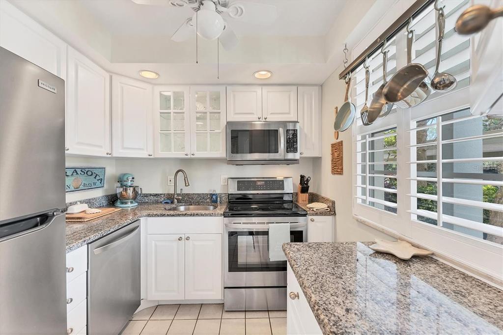 A kitchen features white cabinets, stainless steel appliances, granite countertops, and a hanging pot rack — 4350 CHATHAM DRIVE UNIT 106, LONGBOAT KEY, FL