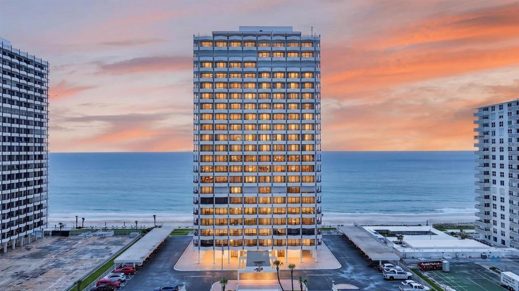 An exterior view of a tall beachfront condominium building at sunset with a parking lot — 2828 N ATLANTIC AVENUE UNIT 1505, DAYTONA BEACH, FL