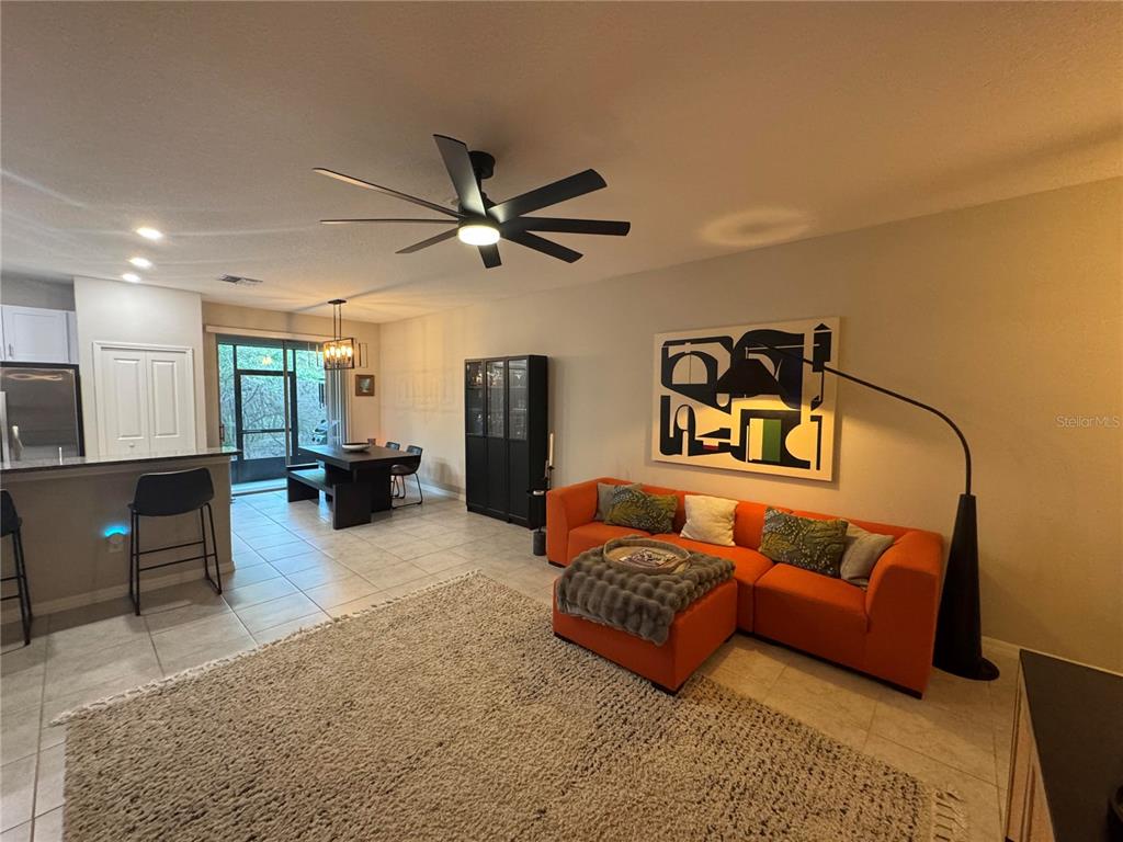 A living room with an orange sofa, a large area rug, and an adjacent dining area — 9640 PEMBROOKE PINES DRIVE, SUN CITY CENTER, FL