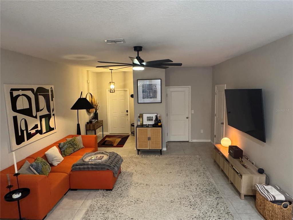 A living room features an orange sectional sofa, a large area rug, and a wall-mounted television — 9640 PEMBROOKE PINES DRIVE, SUN CITY CENTER, FL