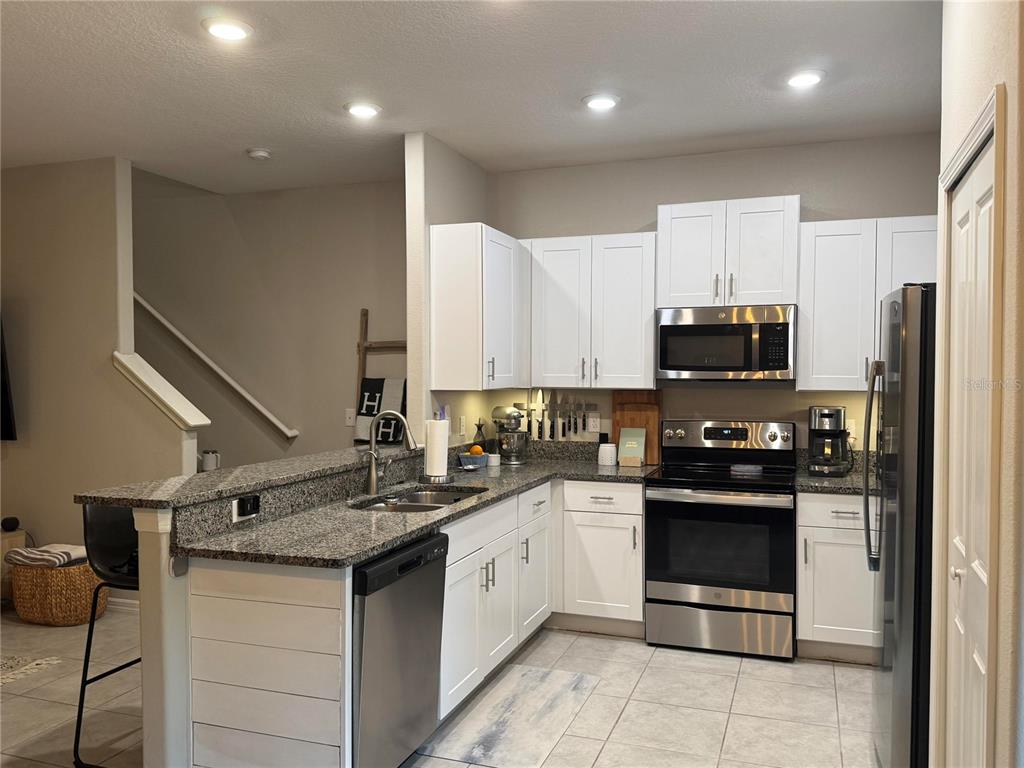 A kitchen features white cabinets, granite countertops, stainless steel appliances, and a breakfast bar — 9640 PEMBROOKE PINES DRIVE, SUN CITY CENTER, FL
