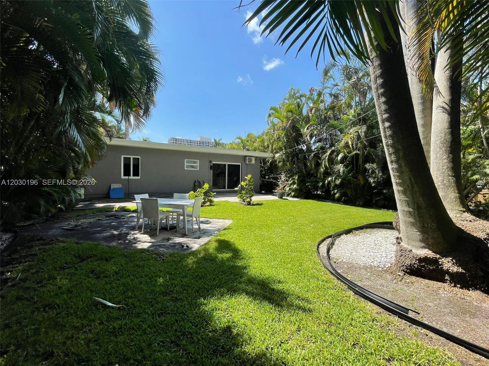A backyard features a patio with a dining set, a lawn, and surrounding palm trees — 1511 NE 109th St, Miami FL 33161, MIAMI, FL