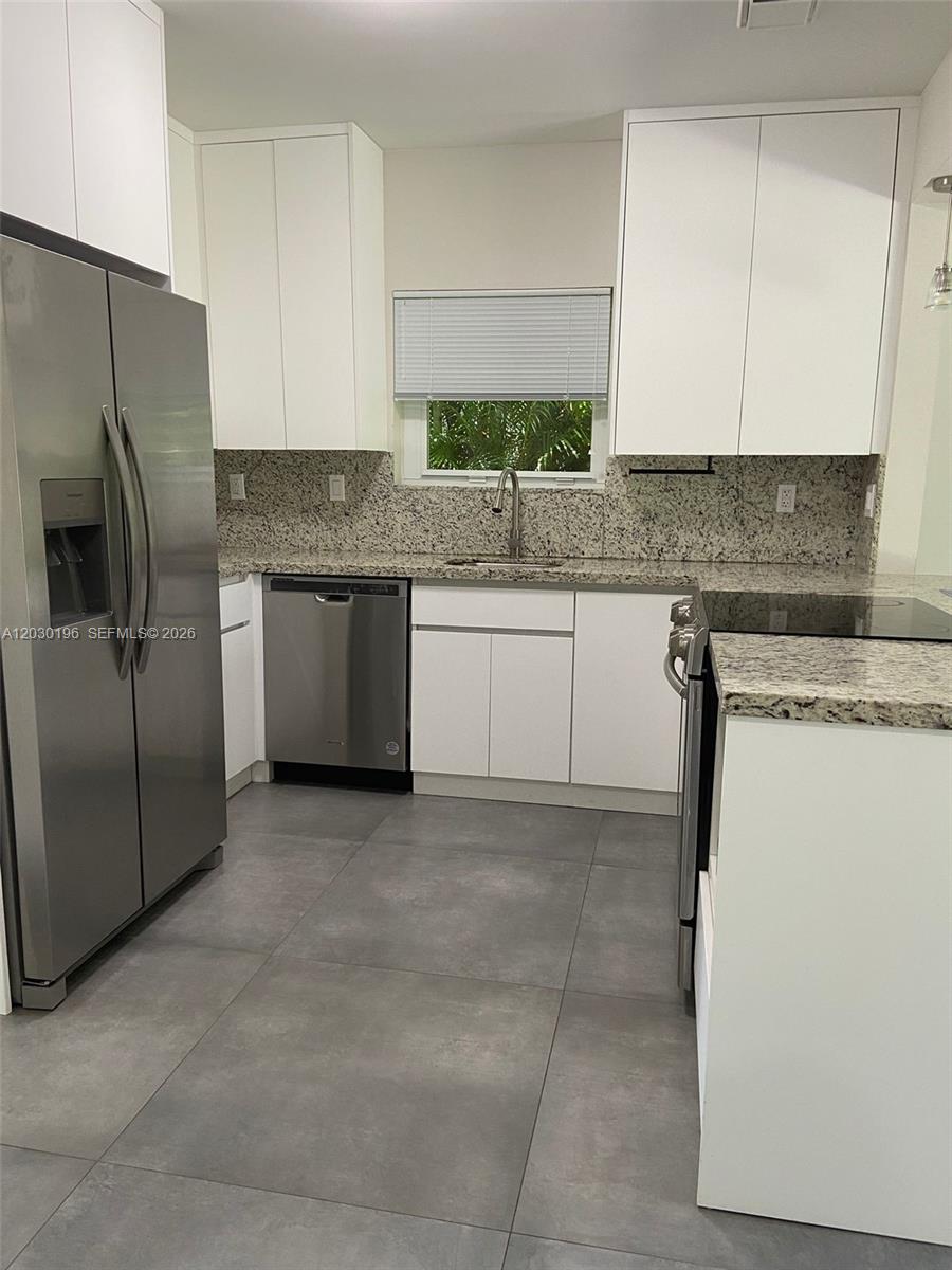 A kitchen features white cabinets, granite countertops, stainless steel appliances, and large gray floor tiles — 1511 NE 109th St, Miami FL 33161, MIAMI, FL