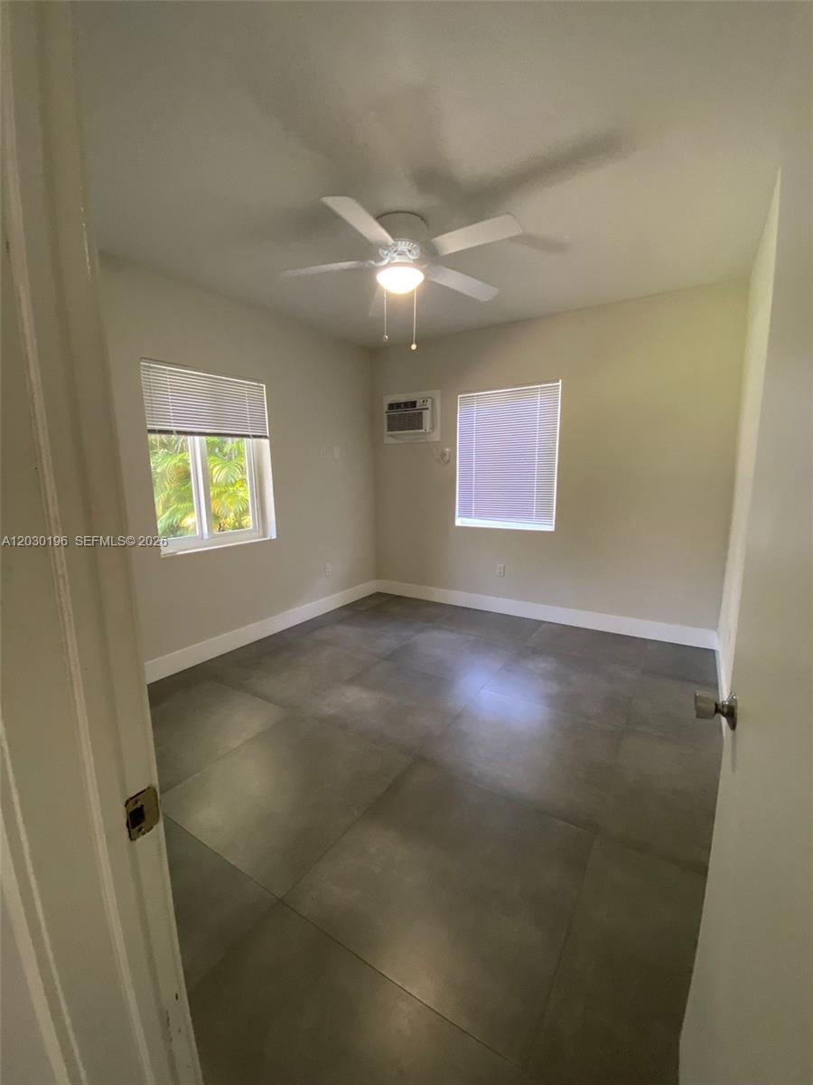 An empty bedroom features large gray floor tiles, a ceiling fan, and two windows — 1511 NE 109th St, Miami FL 33161, MIAMI, FL