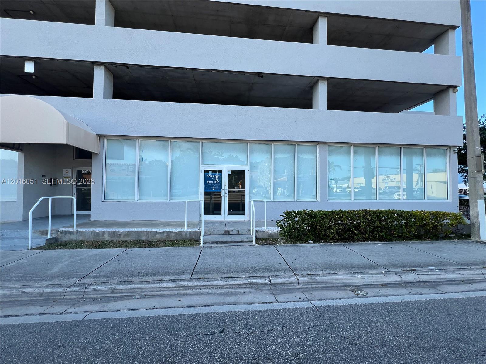 A commercial storefront with large glass windows sits below an open-air concrete parking structure — 2217 NW 7th St # 2, Miami FL 33125, MIAMI, FL
