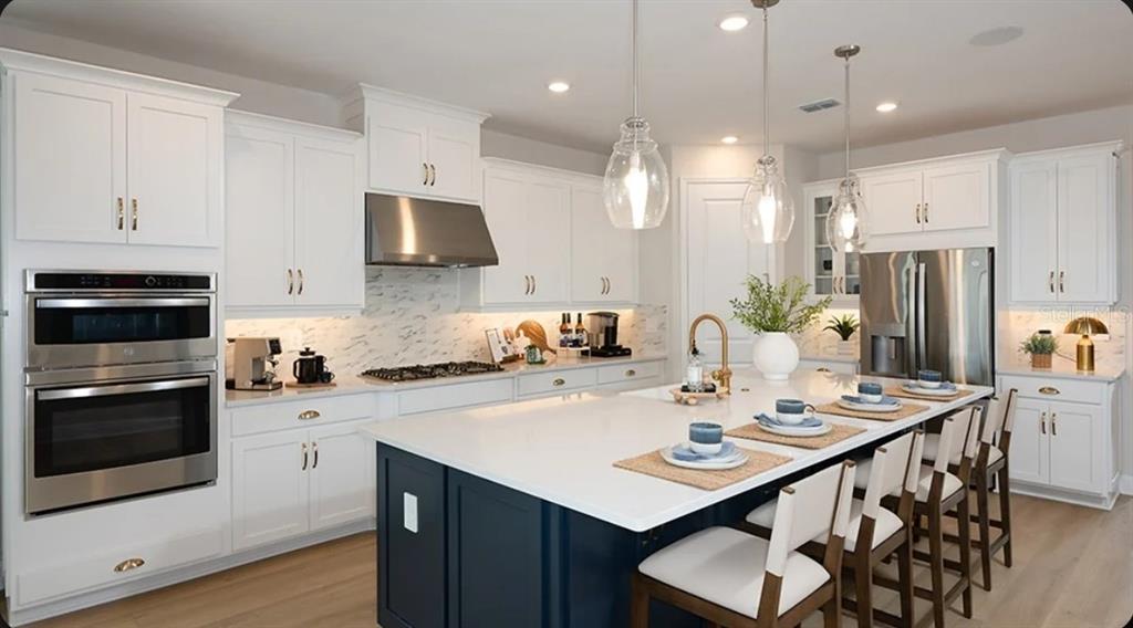 A bright kitchen features white cabinetry, a dark blue island, and stainless steel appliances — 12859 TREELINE RIDGE AVENUE, SAN ANTONIO, FL