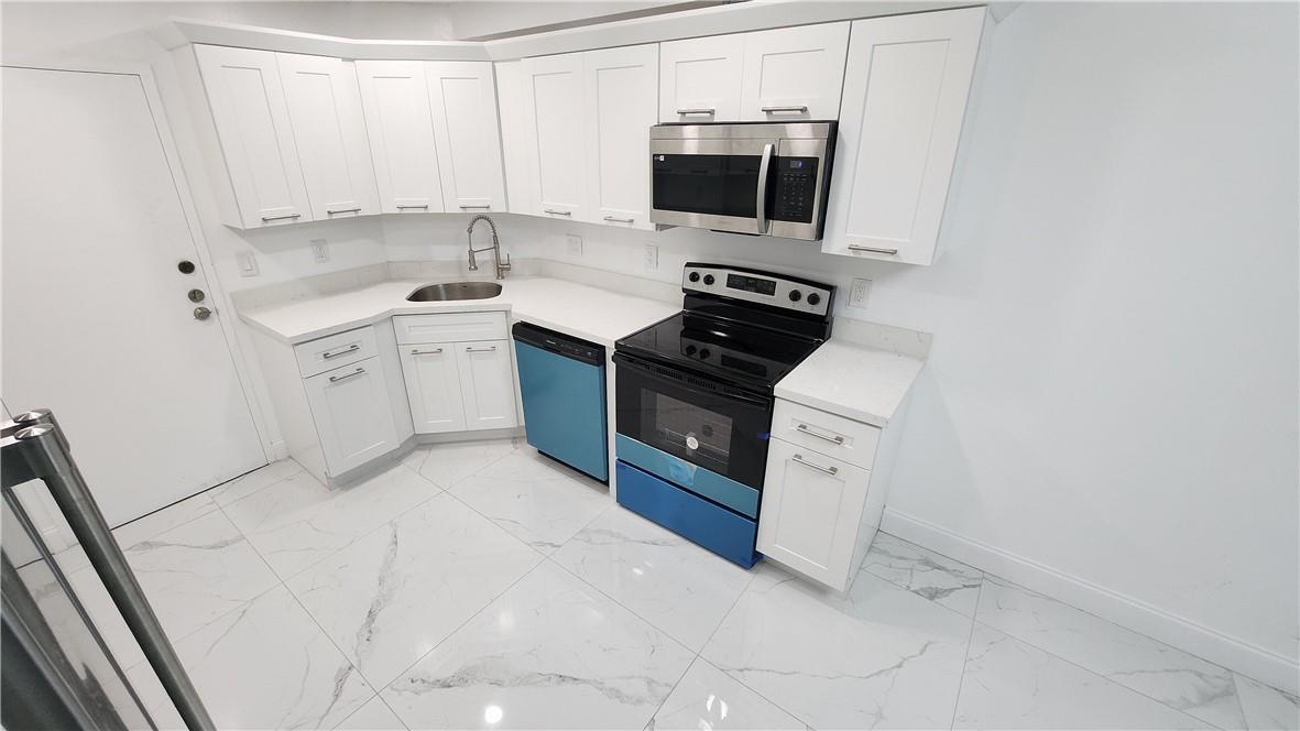 A modern kitchen features white cabinets, stainless steel appliances, and white marble-patterned tile flooring — 3301 Spanish Moss Terrace # 202, Lauderhill FL 33319, LAUDERHILL, FL