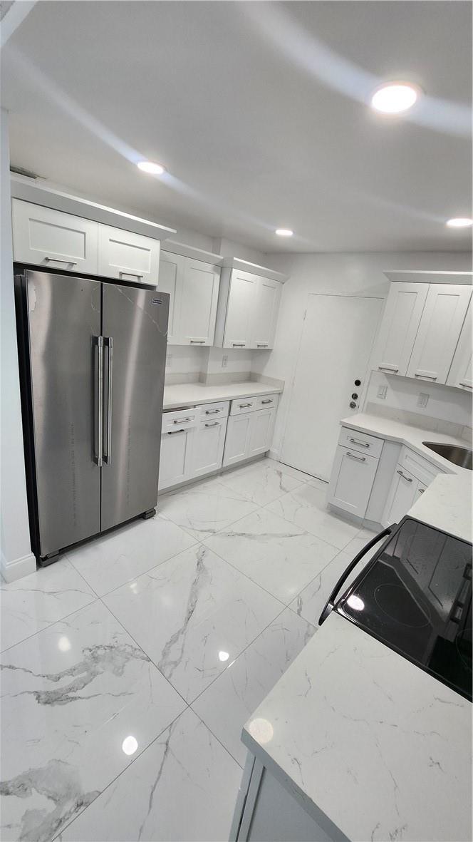 A modern kitchen features white cabinets, stainless steel appliances, and white marble-patterned tile flooring — 3301 Spanish Moss Terrace # 202, Lauderhill FL 33319, LAUDERHILL, FL
