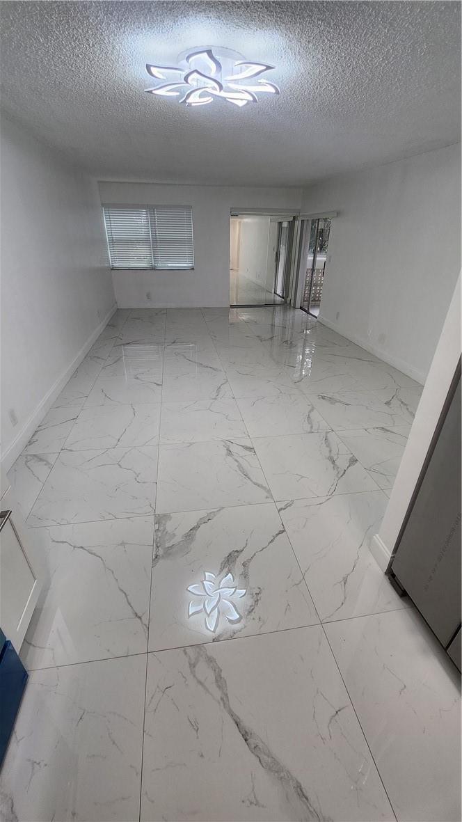 An empty room features white marble-look floor tiles, white walls, and a modern ceiling light — 3301 Spanish Moss Terrace # 202, Lauderhill FL 33319, LAUDERHILL, FL