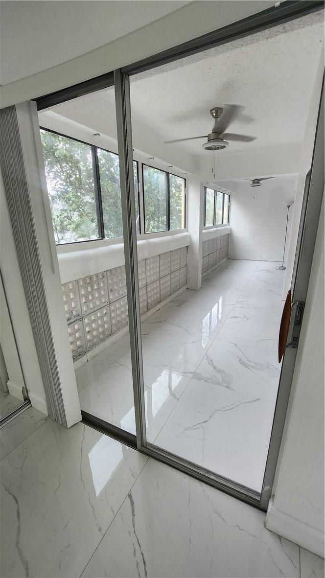 A sunroom with white marble-look tile flooring, glass sliding doors, and a glass block wall — 3301 Spanish Moss Terrace # 202, Lauderhill FL 33319, LAUDERHILL, FL