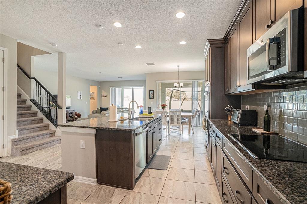 A kitchen features dark wood cabinets, granite countertops, stainless steel appliances, and a central island — 13362 SAGE HOLLOW AVENUE, RIVERVIEW, FL