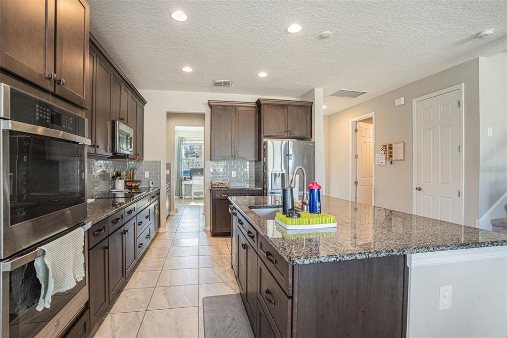 A kitchen features dark wood cabinets, granite countertops, stainless steel appliances, and a central island — 13362 SAGE HOLLOW AVENUE, RIVERVIEW, FL