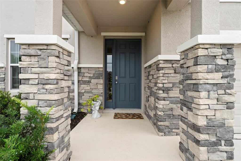 A covered entryway features a dark blue front door flanked by stone-clad support columns — 2136 MIDNIGHT PEARL DRIVE, SARASOTA, FL