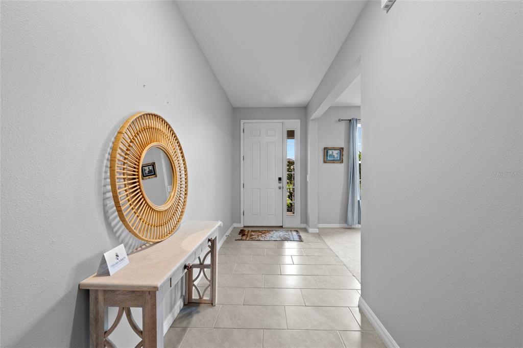 A bright entryway features light tile flooring, a white front door, and a rattan mirror — 2136 MIDNIGHT PEARL DRIVE, SARASOTA, FL
