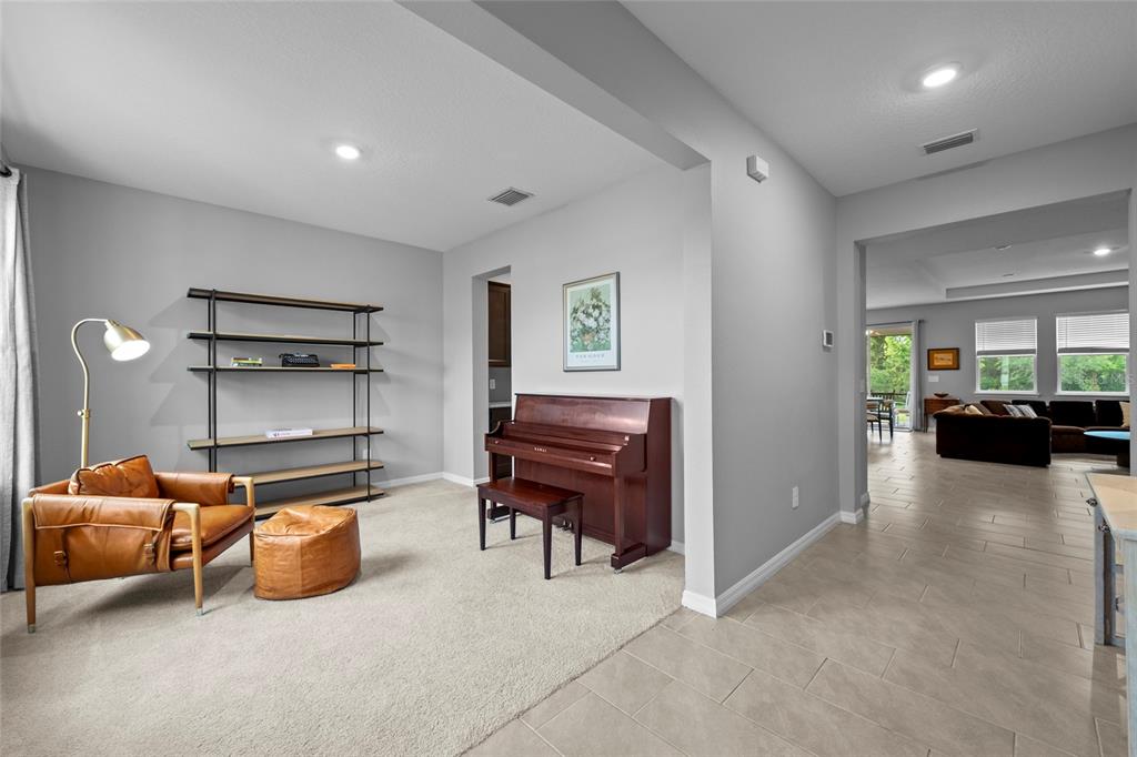 A living area features a piano, a leather armchair, and a bookshelf on carpeted flooring — 2136 MIDNIGHT PEARL DRIVE, SARASOTA, FL