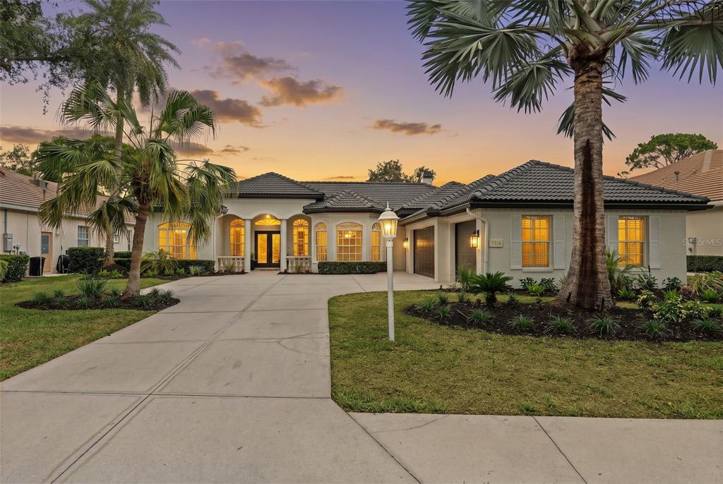 A single-story house with a tile roof, arched windows, and a concrete driveway at sunset — 7318 EATON COURT, UNIVERSITY PARK, FL